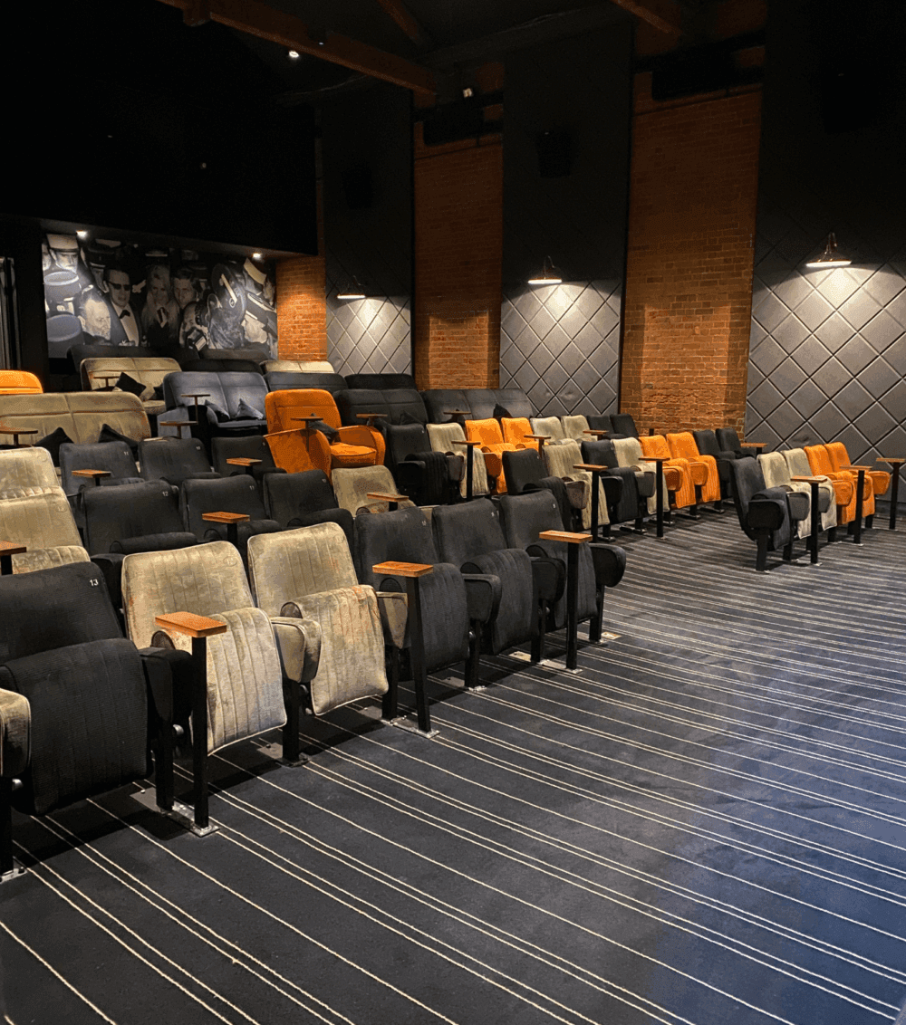 Empty theatre with eclectic, vintage seating in various colors and a black and white striped carpet everyman cinema Winchester. - Home Instead