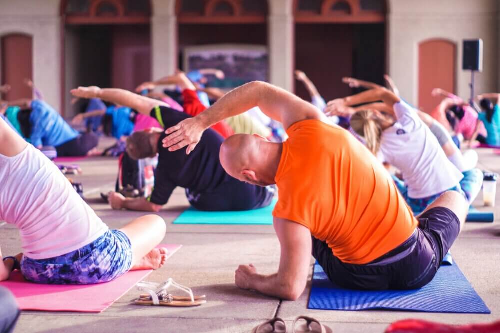 People participating in a group yoga class, performing a side stretch on colorful mats indoors. - Home Instead