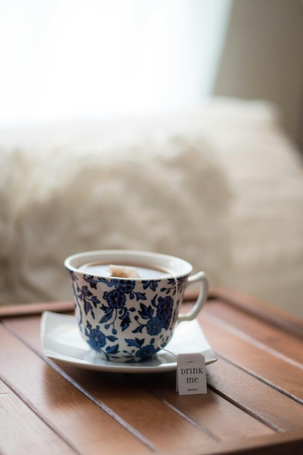 A floral teacup with a tea bag labeled "drink me" on a wooden tray, with a soft, blurred background. - Home Instead
