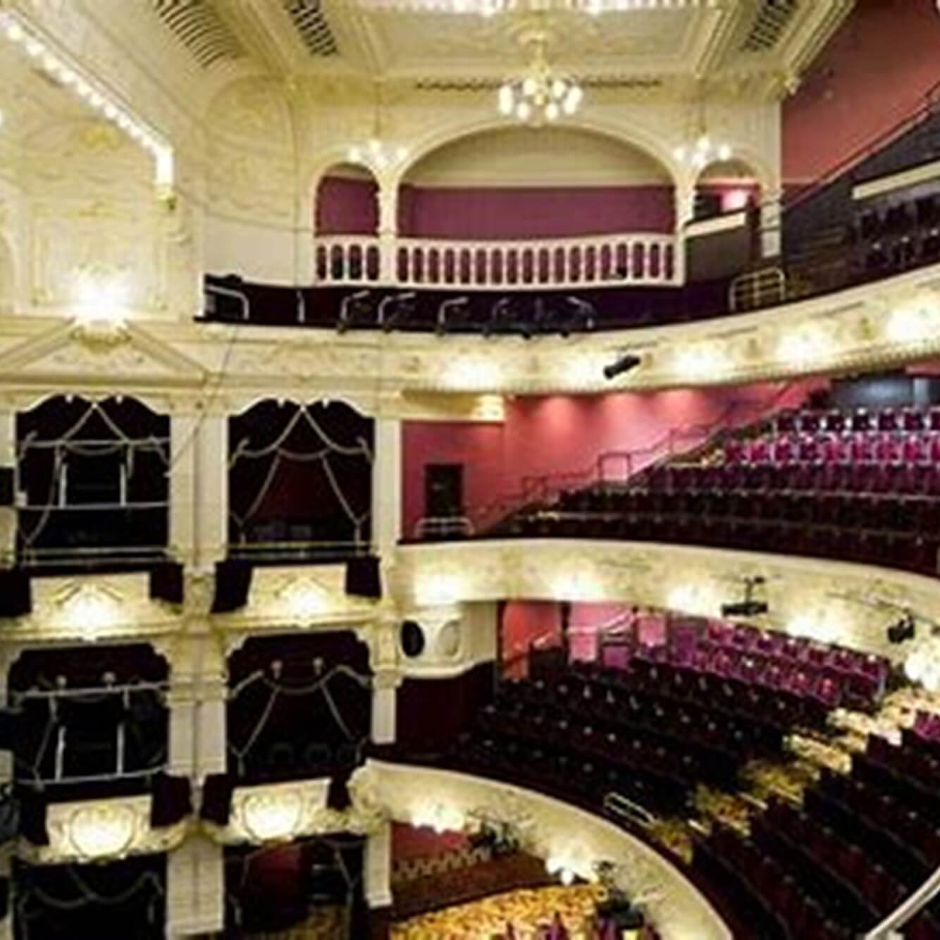 Interior of an elegant theater with ornate balconies and red seating, featuring multiple tiers and bright lighting. - Home Instead