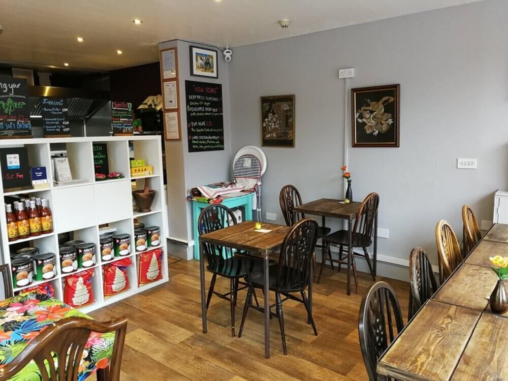Cozy café with wooden tables and chairs, decorative wall art, shelves with canned goods, and a colorful counter area. - Home Instead