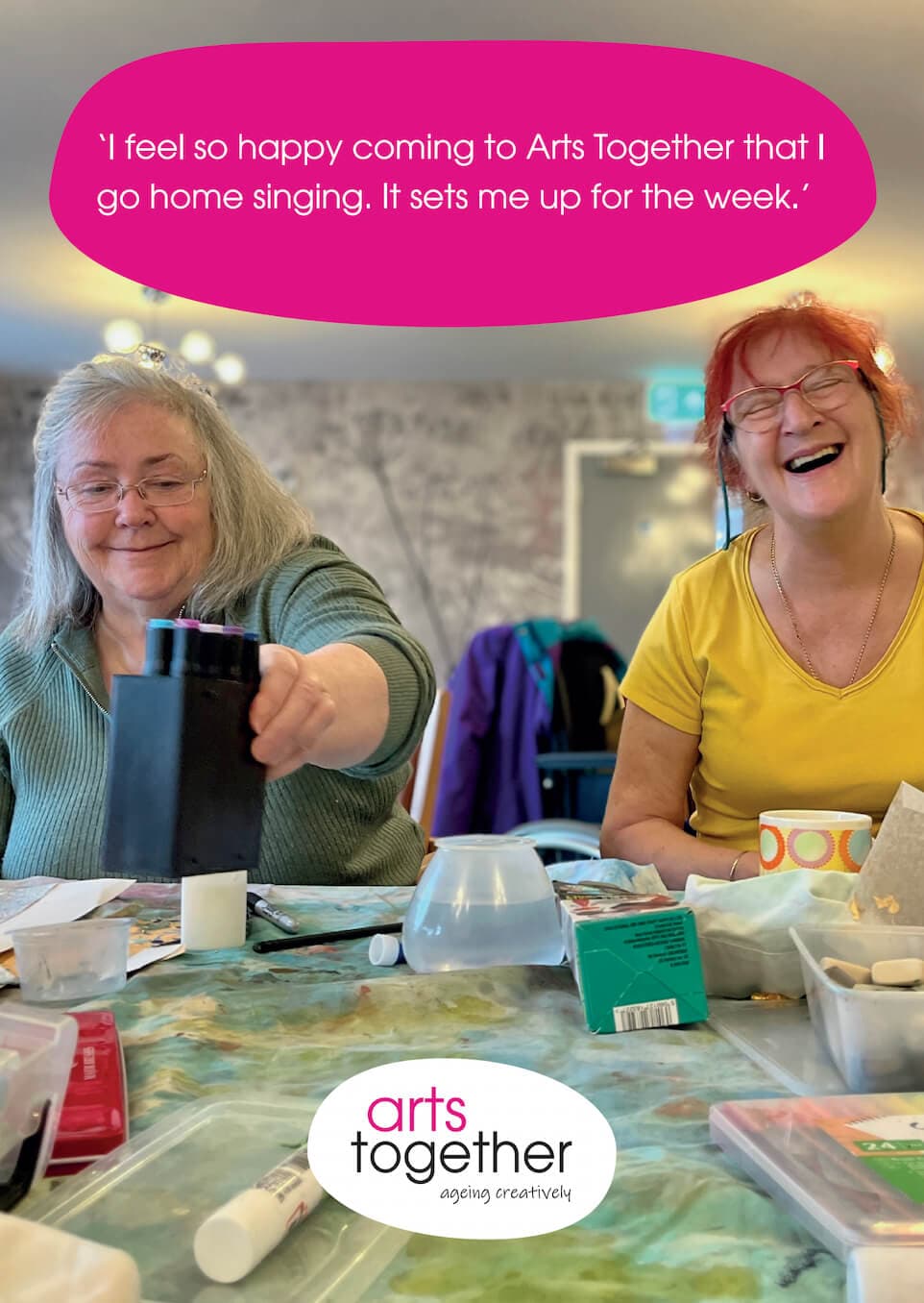 Two smiling women enjoy arts and crafts at a table with the text: 'I feel so happy coming to Arts Together...'. - Home Instead