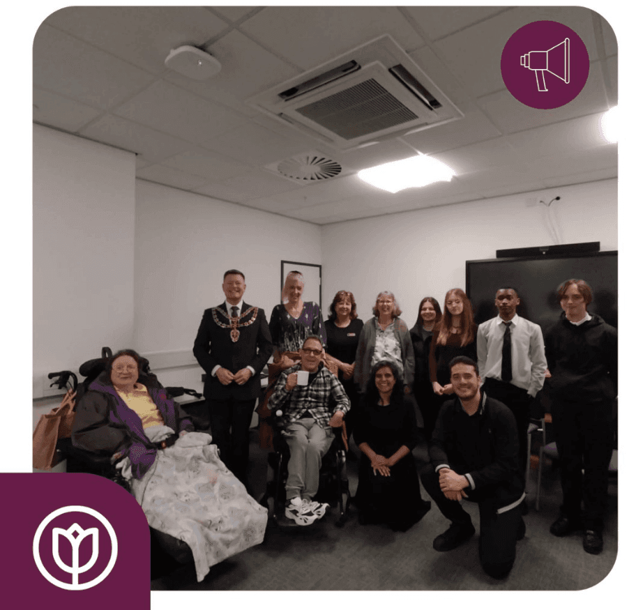 A group of people, including some in wheelchairs, are posing together in an indoor setting with white walls. - Home Instead