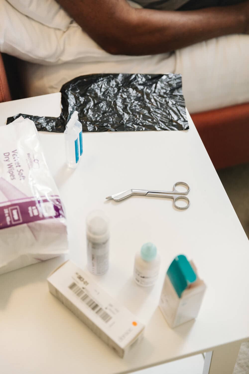 Medical supplies including scissors, wipes, and medications on a table near a person's arm. - Home Instead