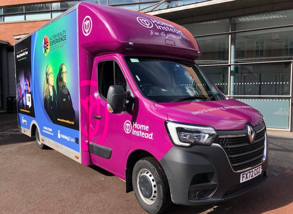 A bright purple Home Instead van with advertisements and branding is parked outside a building. - Home Instead