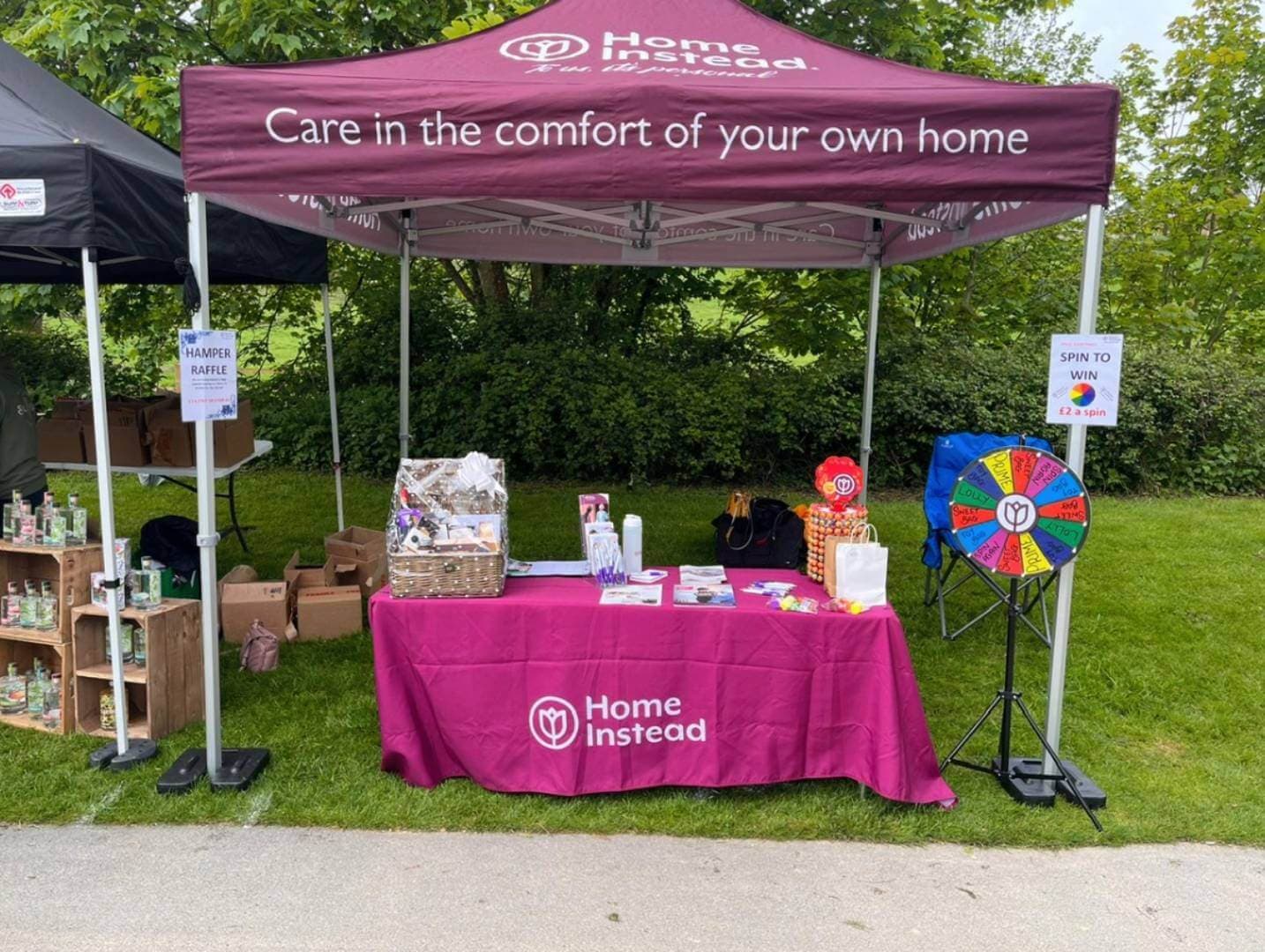 Home Instead booth at an outdoor event with promotional materials, a spinning wheel game, and a purple tablecloth. - Home Instead