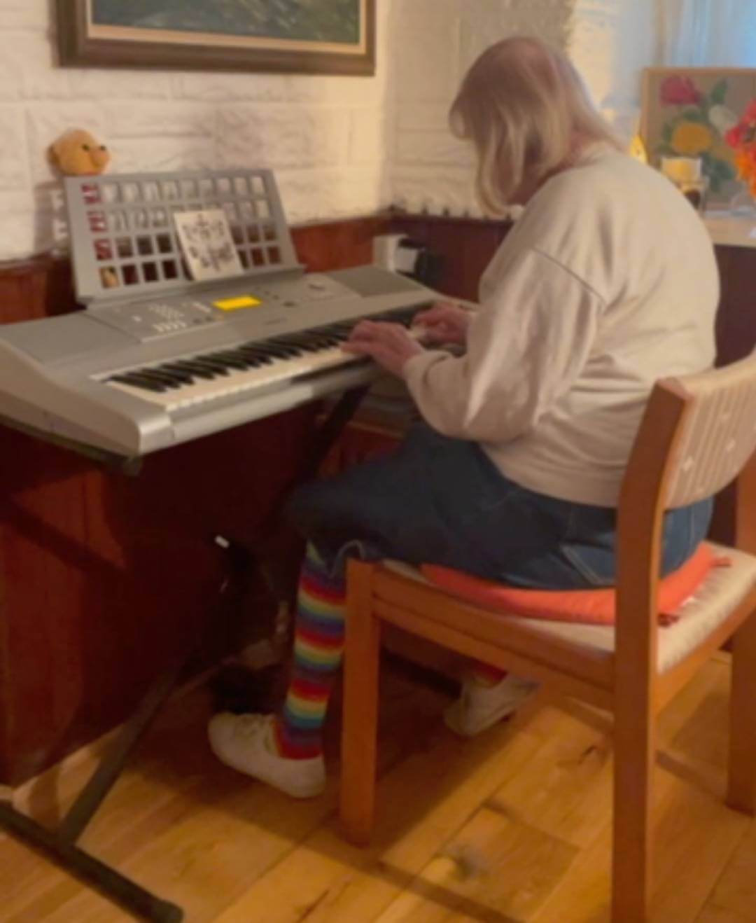 Person in a white sweater and colorful striped socks playing an electronic keyboard while sitting on a wooden chair. - Home Instead