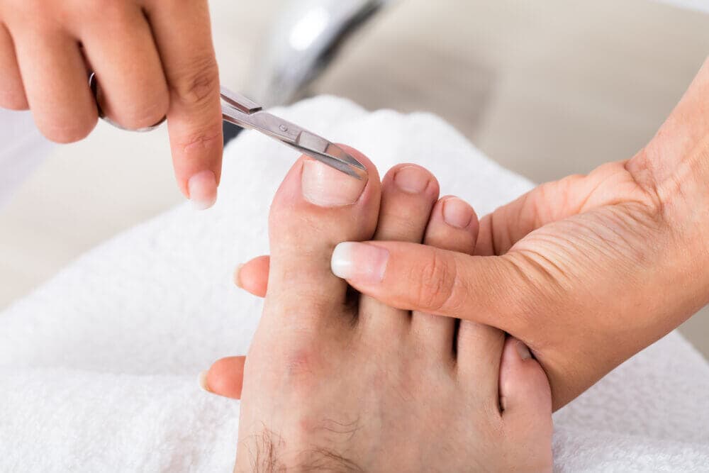 Close-up of a person receiving a pedicure, with focus on hands clipping toenails with nail clippers. - Home Instead