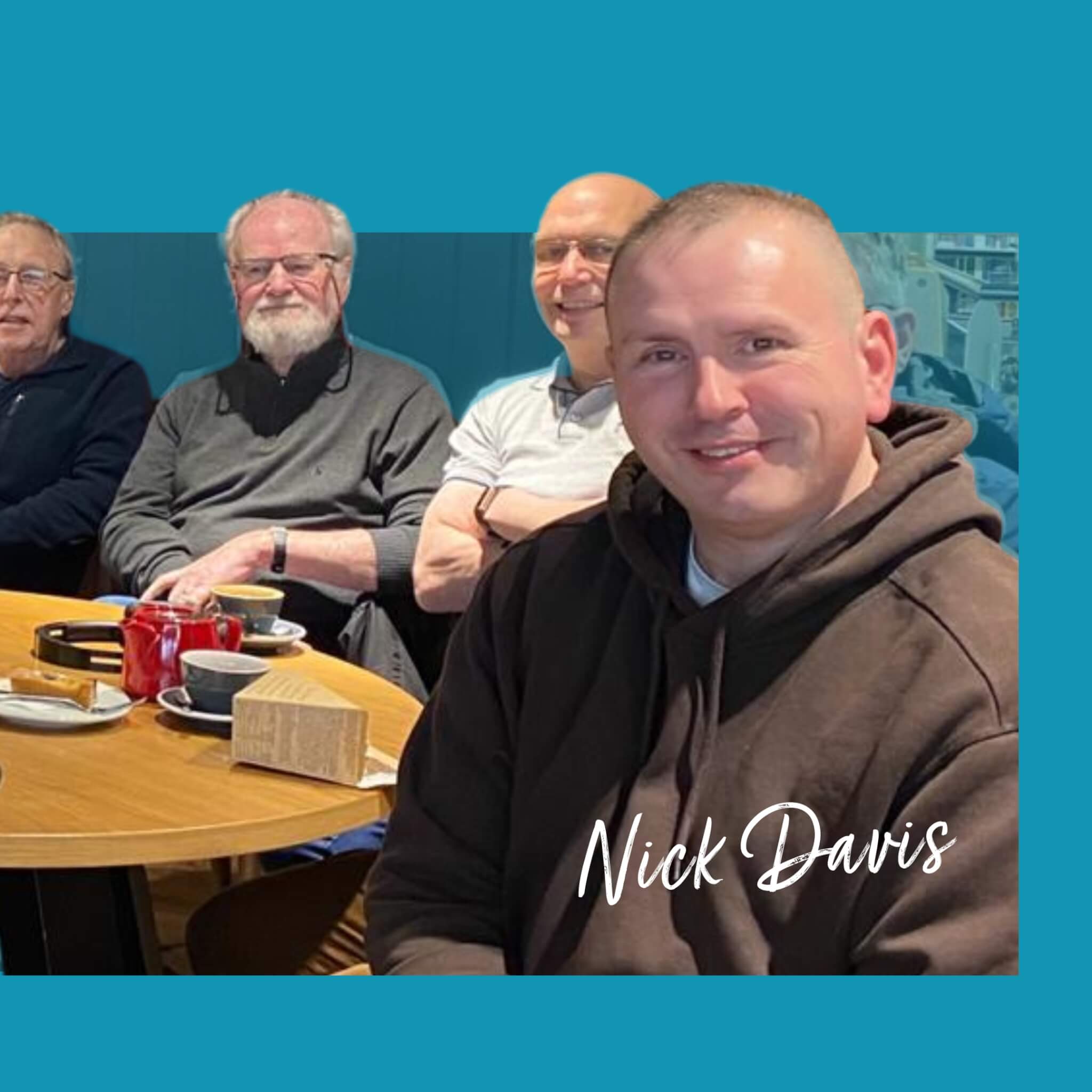 Four men sitting at a table with drinks, focused on the man in front wearing a brown hoodie, labeled "Nick Davis. - Home Instead