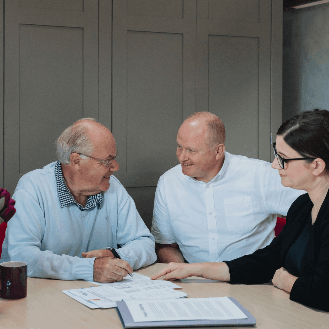 A Home Instead client is reading through paperwork with two other people, all seated at a table.