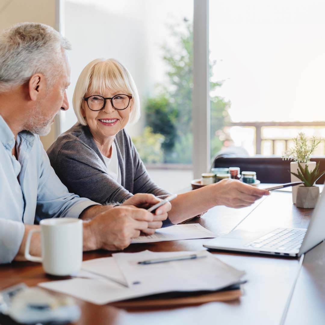 older couple reviewing documents and looking at information on laptop