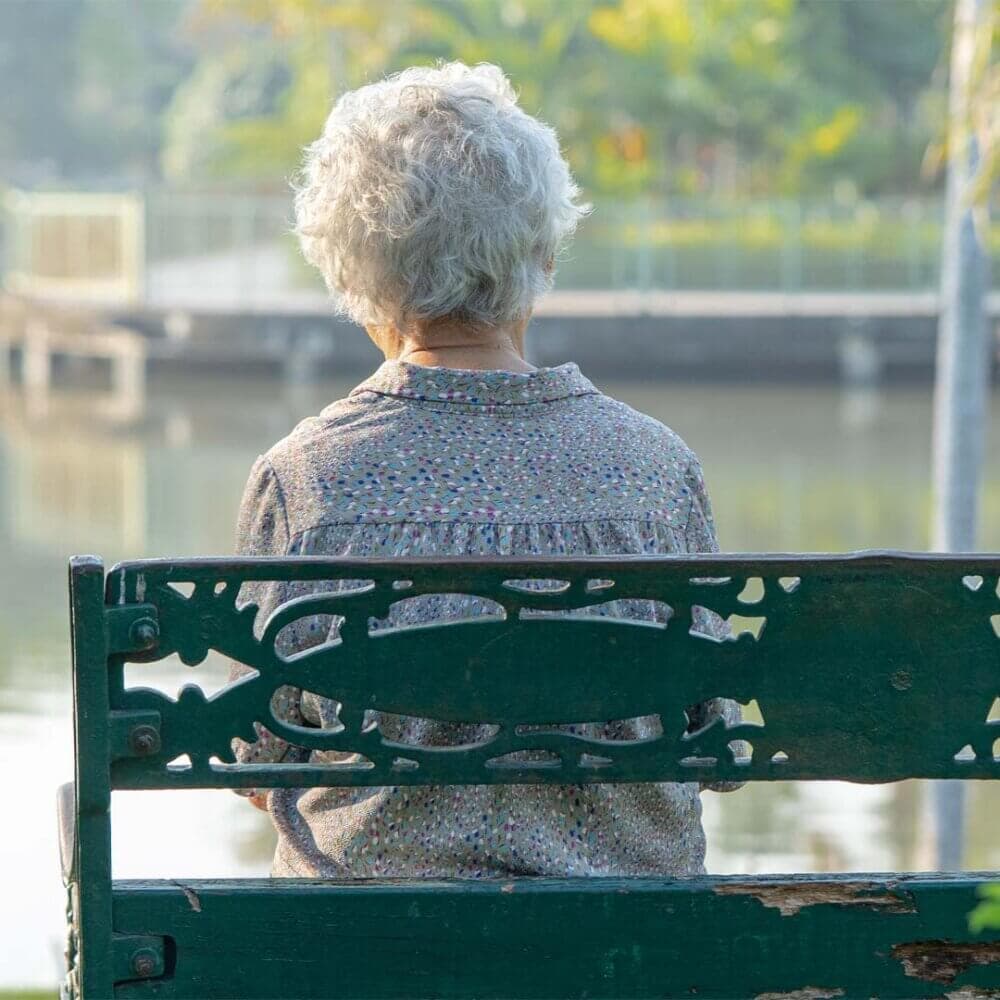 older lady sitting alone on a bench looking out over an area of water