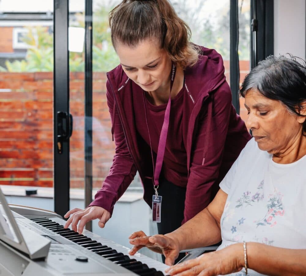 Senior woman playing the piano inside the house with her carer