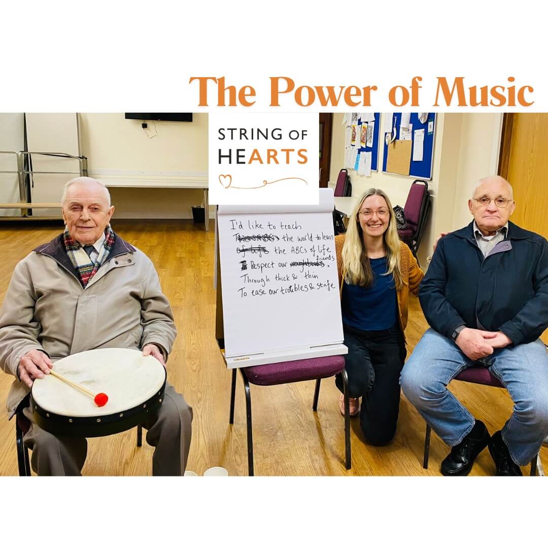 Three people smiling, one holding a drum, sitting beside an easel with handwritten text under "String of Hearts. - Home Instead