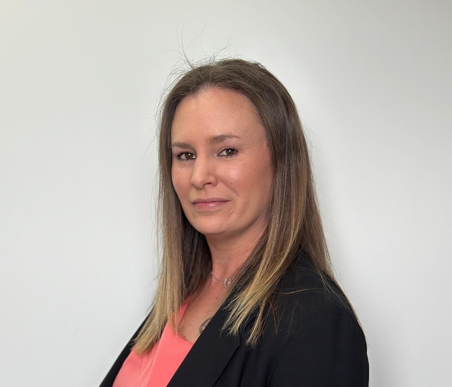 A woman with long straight hair wearing a black blazer and pink top against a plain white background. - Home Instead