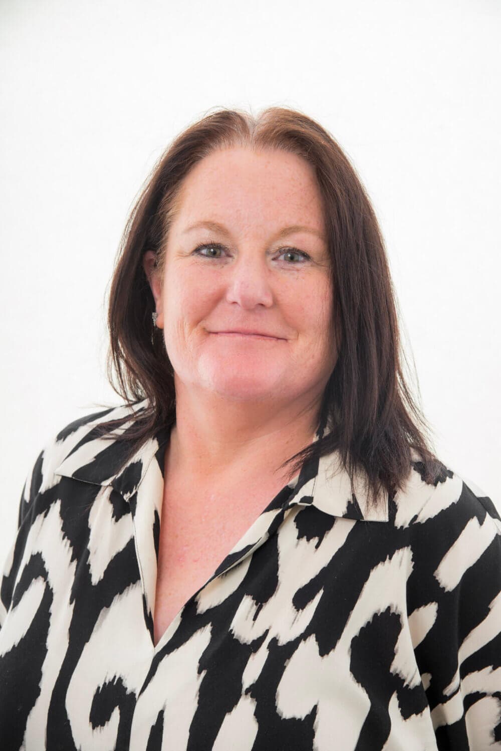 Woman with long dark hair wearing a black and white patterned blouse, smiling against a plain white background. - Home Instead