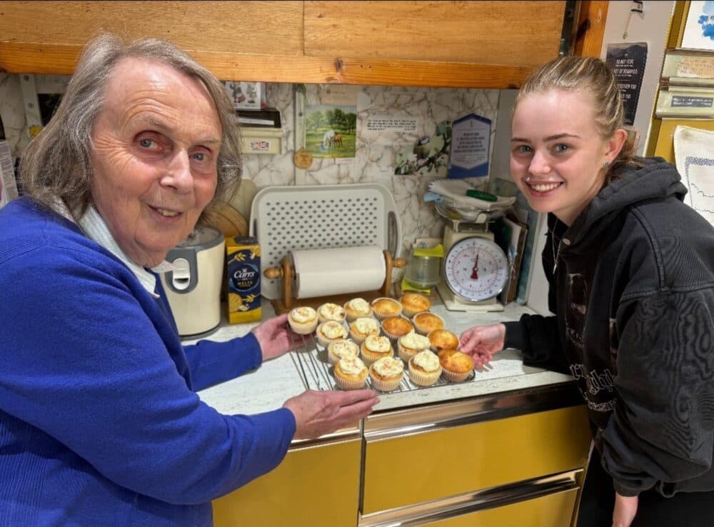 Two women smiling and showing baked cupcakes in a rustic kitchen. - Home Instead