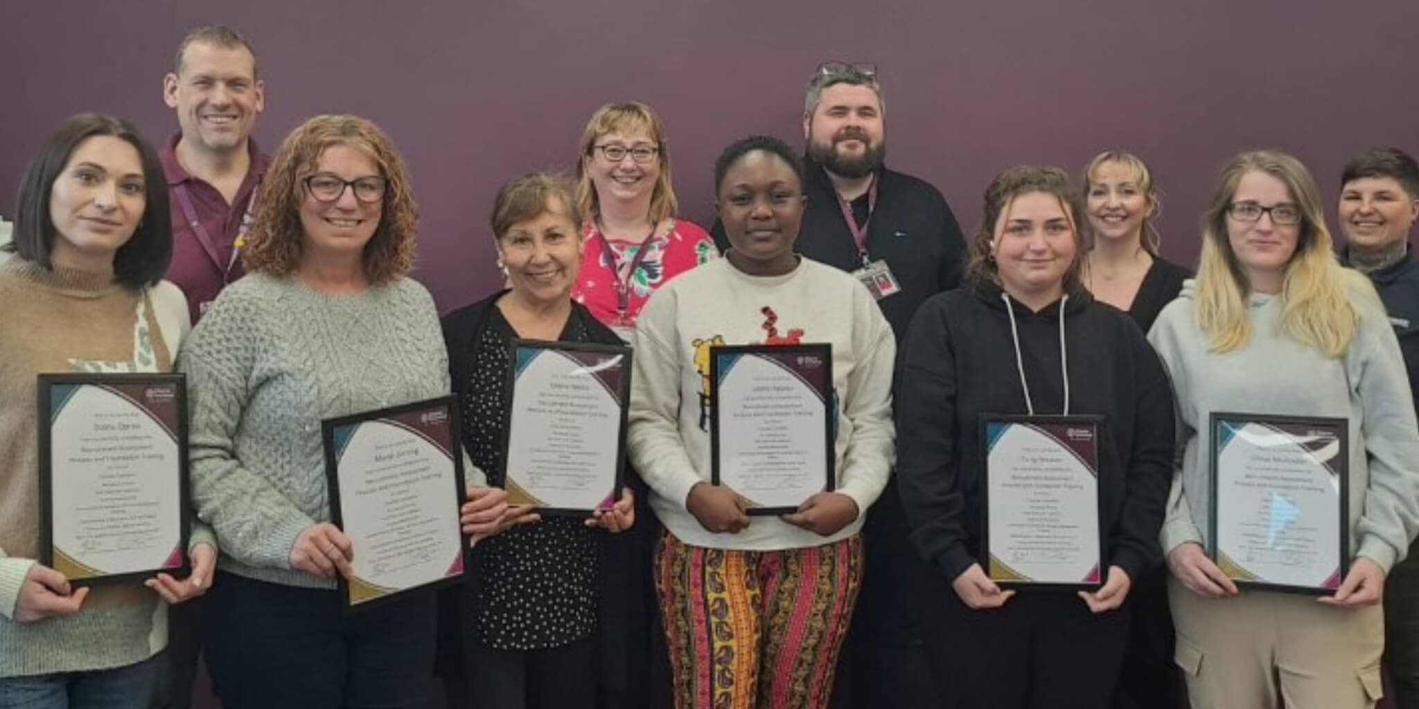 A group of people standing and holding certificates, posing for a photo against a purple background. - Home Instead