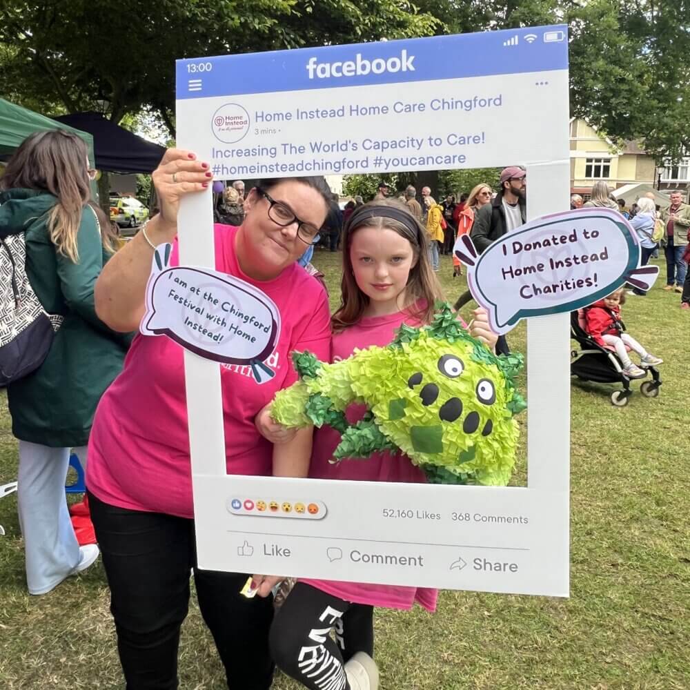 Two people holding signs and a green monster piñata in a Facebook frame promoting a Home Care charity event. - Home Instead