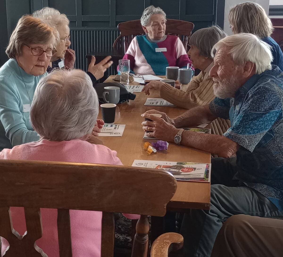 Group of elderly people sitting around a table, engaging in conversation and drinking coffee. - Home Instead