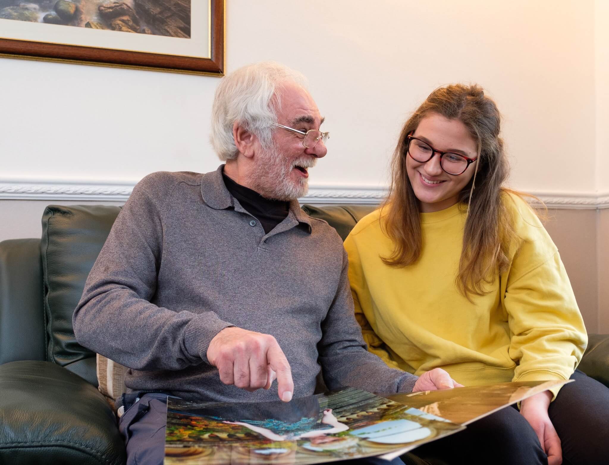 Home Instead client and his granddaughter sitting on a settee and looking at a photo album