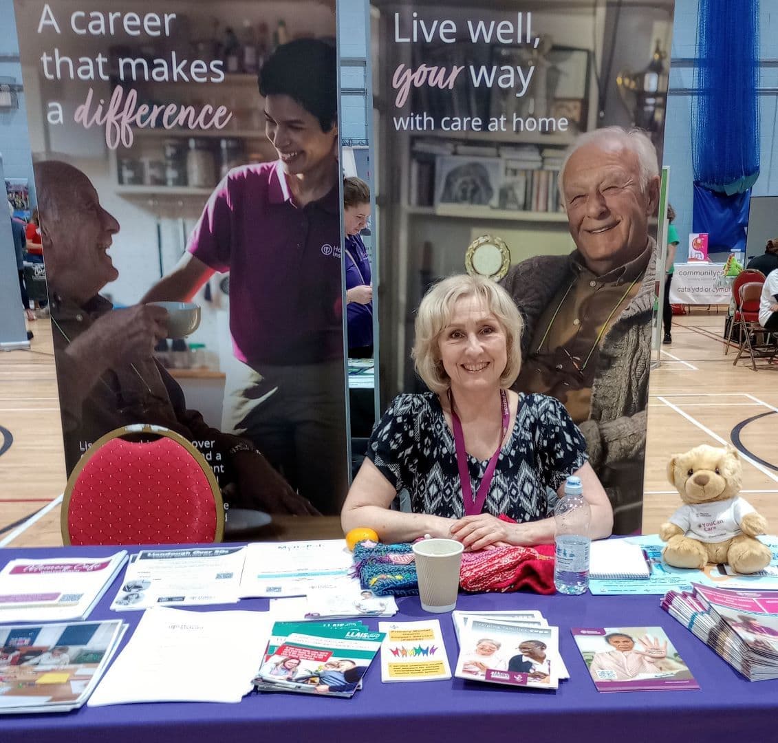 Woman sitting at a booth with brochures and posters promoting careers in home health care at a community event. - Home Instead