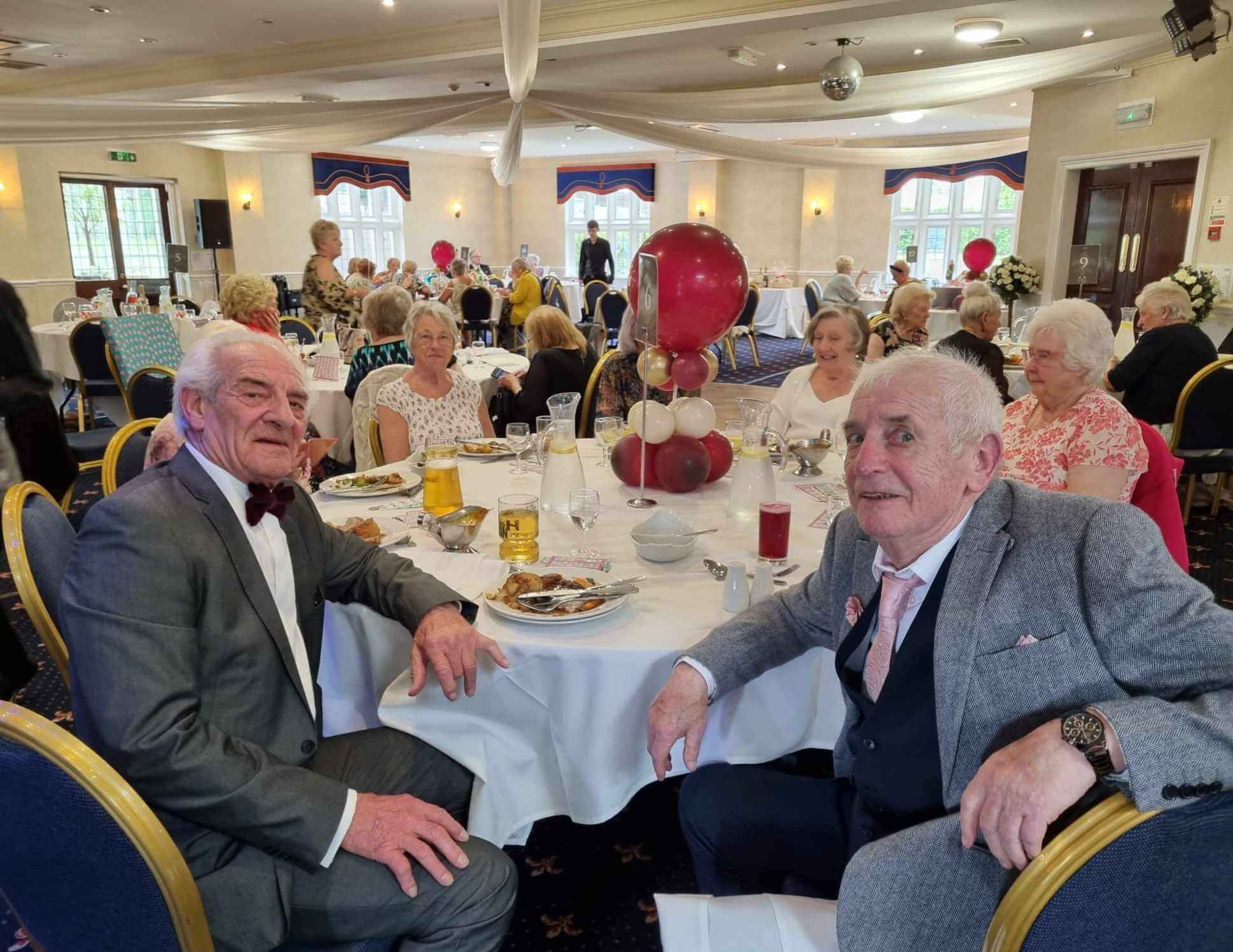 Elderly people seated at decorated tables, enjoying a formal gathering or event in a banquet hall. - Home Instead