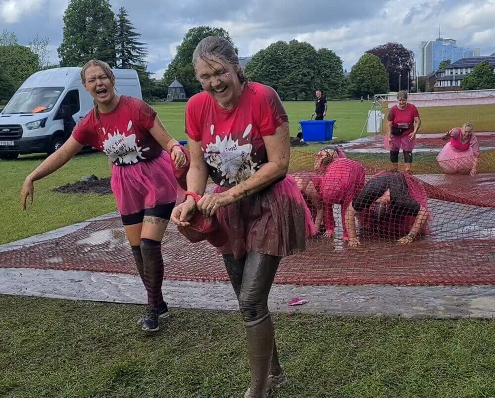 Home Instead participants Jess and Lynn emerging from under the netting wet and muddy