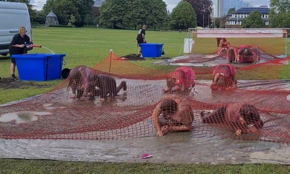 Participants in "Race For Life Pretty Muddy" crawl through water and mud under netting