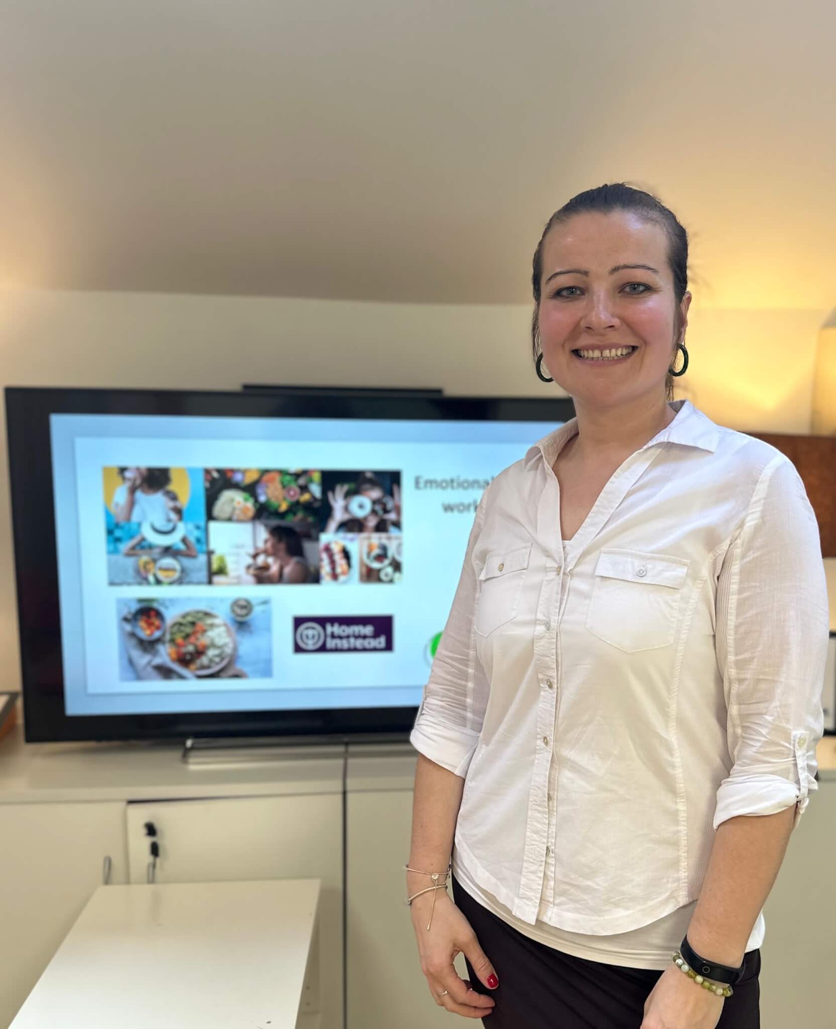 A person standing in front of a presentation screen showing a slide with food images and the "Home Instead" logo. - Home Instead