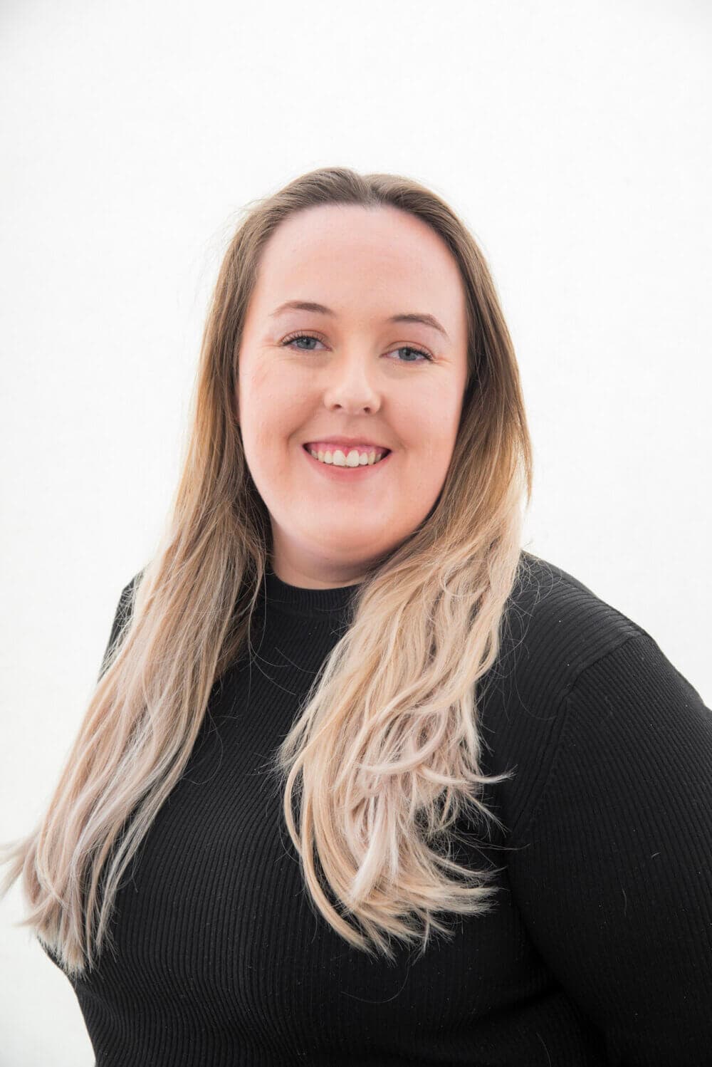 A smiling woman with long, blonde hair wearing a black top against a plain white background. - Home Instead