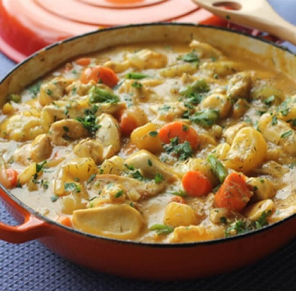 A vibrant orange cast iron skillet filled with a colorful vegetable and chicken stew, garnished with fresh herbs. - Home Instead