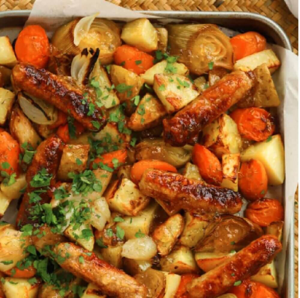 Sheet pan of roasted sausages, potatoes, carrots, onions, and garnished with chopped parsley. - Home Instead