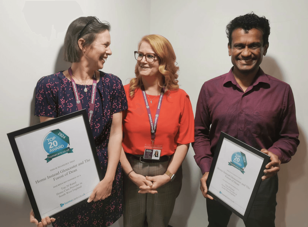 Jo, Sharon and Deepak from the Home Instead Gloucester office smiling and holding framed homecare top 20 awards.