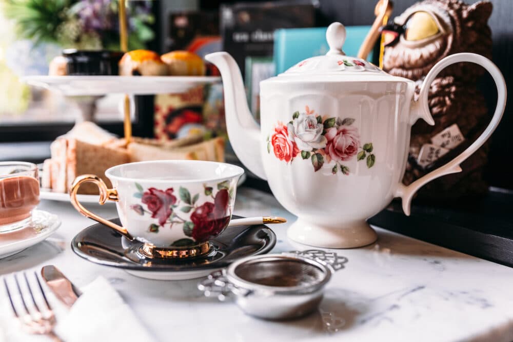 Teapot and cup with floral designs on a marble table next to a tea strainer, pastries, and an owl figurine. - Home Instead