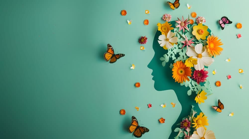 Silhouette of a person's profile made from colorful flowers and butterflies against a teal background. - Home Instead