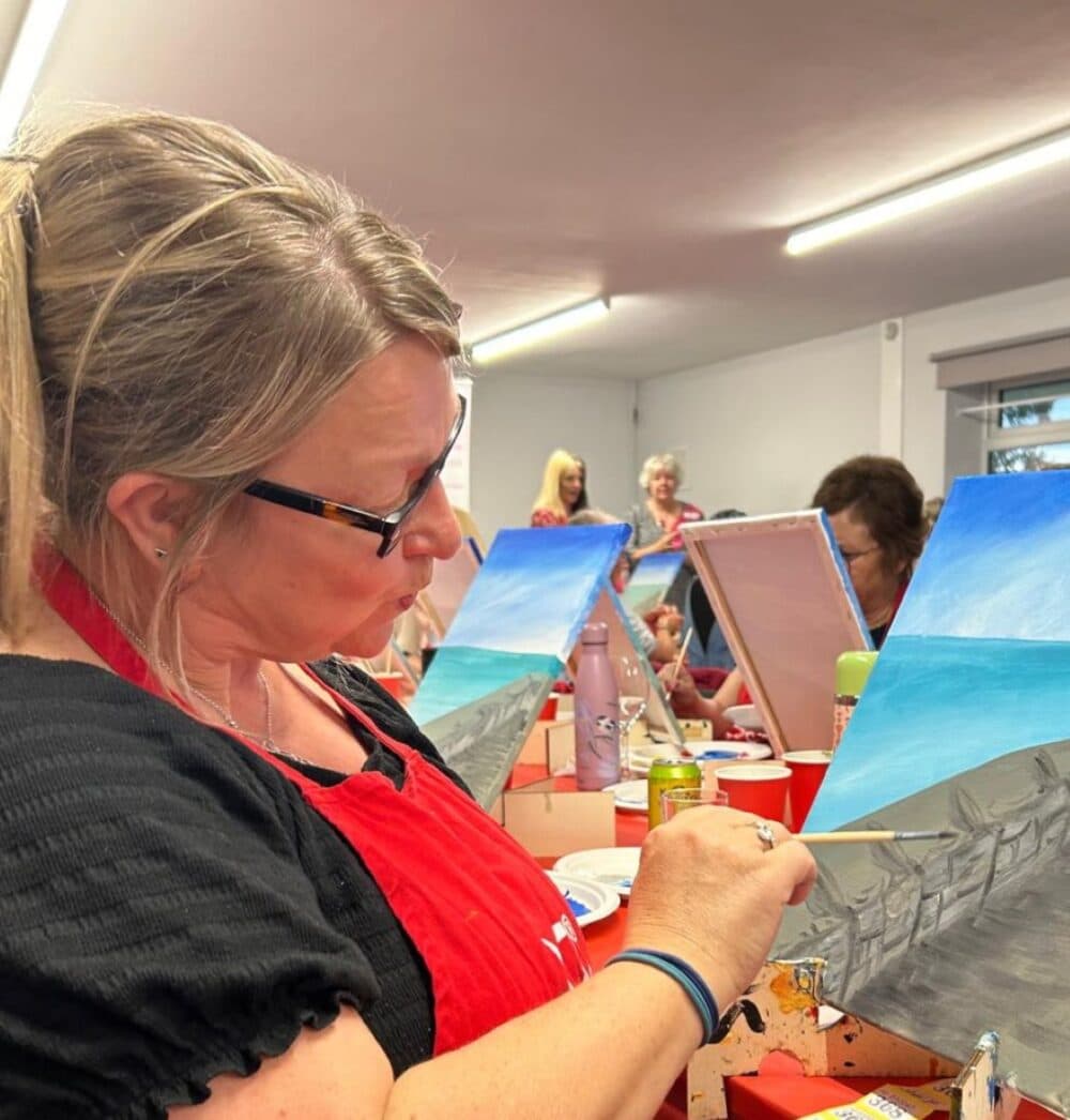 Dee painting at her easel, looking professional