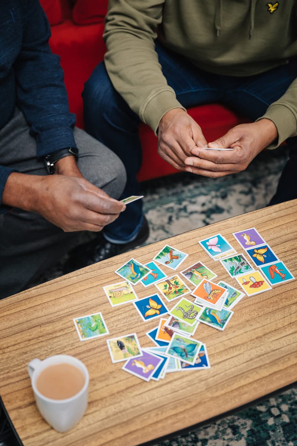 Two people sorting colorful stickers on a wooden table with a mug of tea nearby. - Home Instead