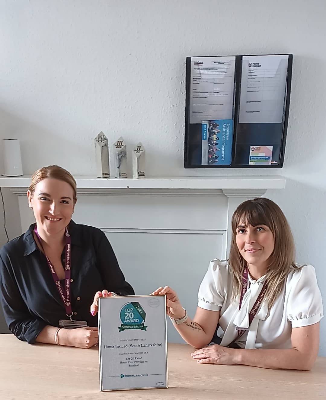 Two women smiling at a table, one holding a framed "Top 20 Home Care 2023 Award". - Home Instead