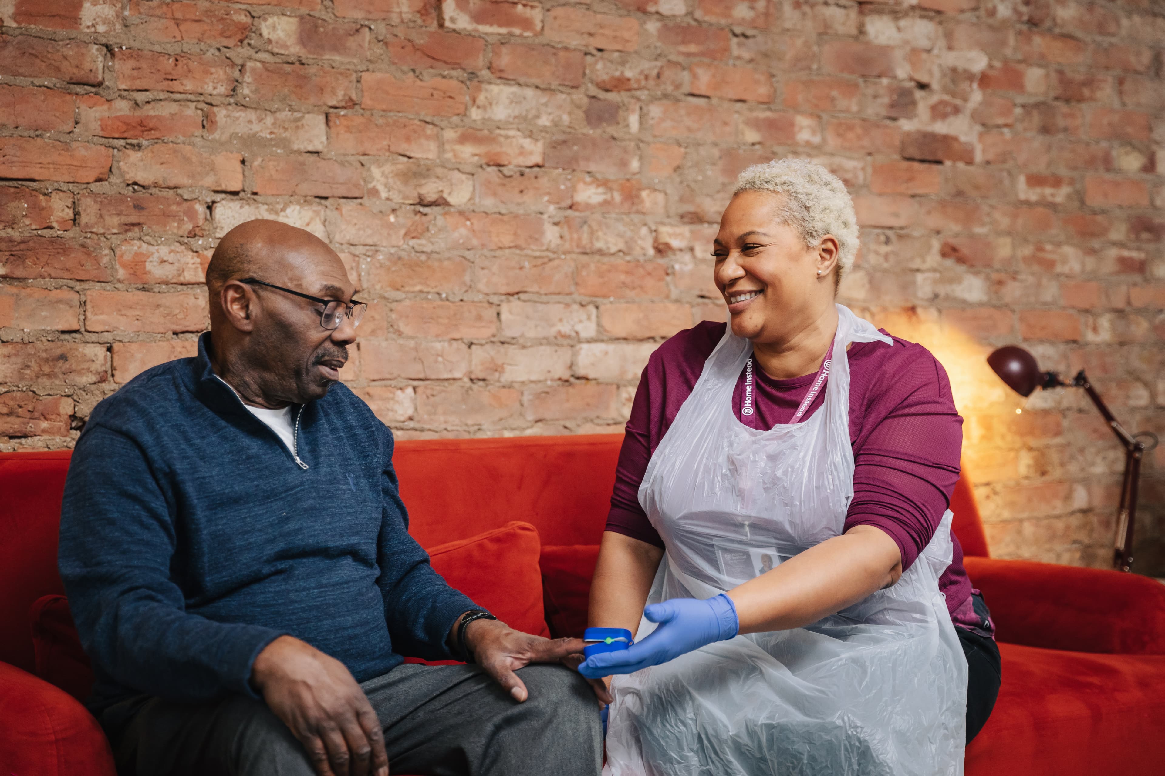 Home Instead Care Pro sits on sofa with client and checks his blood oxygen levels