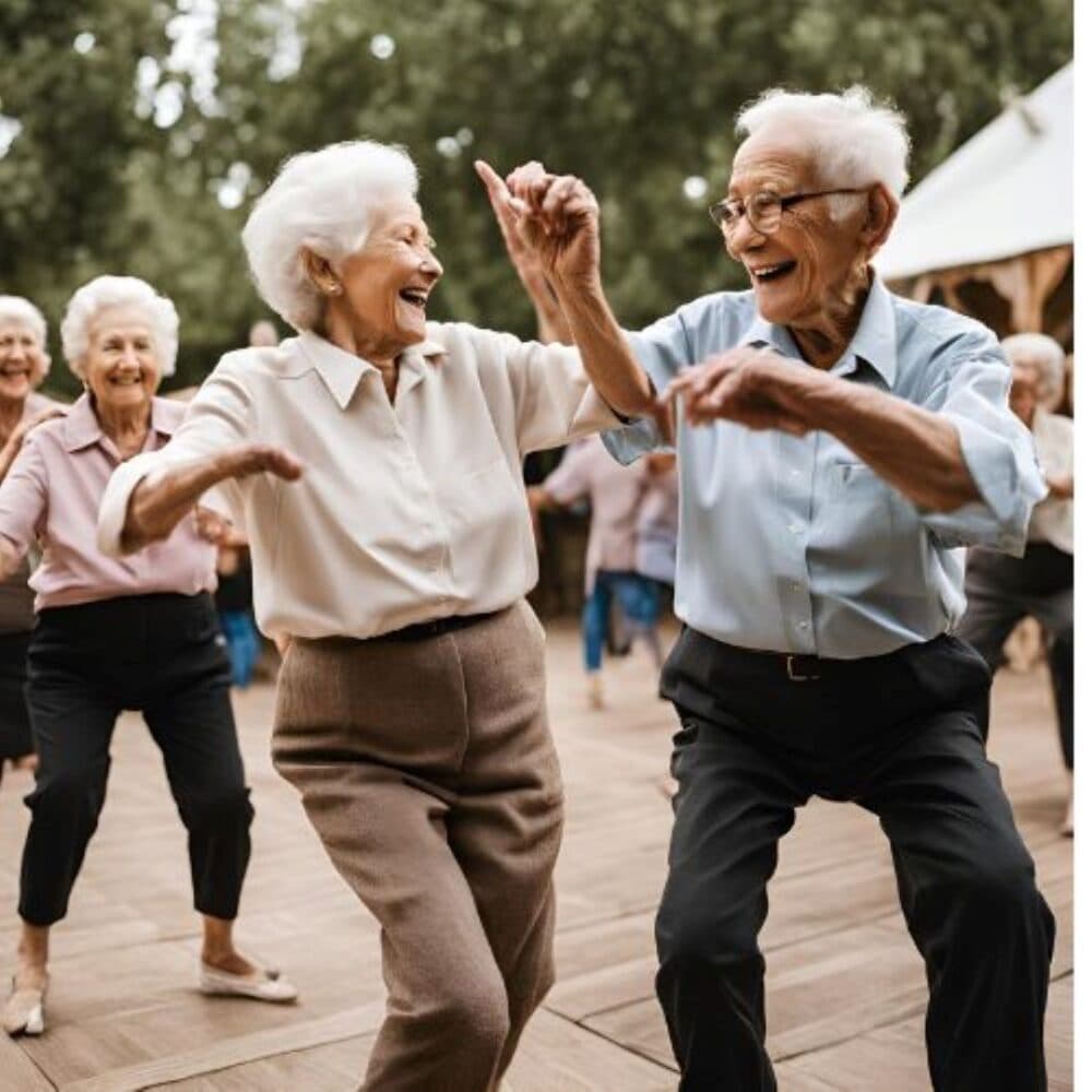 Elderly group joyfully dancing outdoors, wearing casual clothing, with trees and a tent in the background. - Home Instead