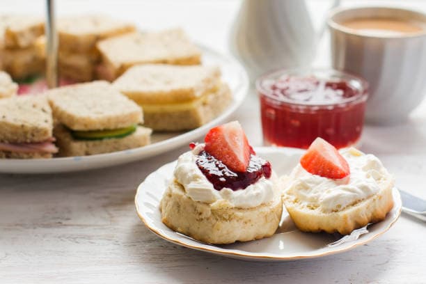 Scones topped with cream and strawberries, sandwiches, and a cup of coffee on a table. - Home Instead