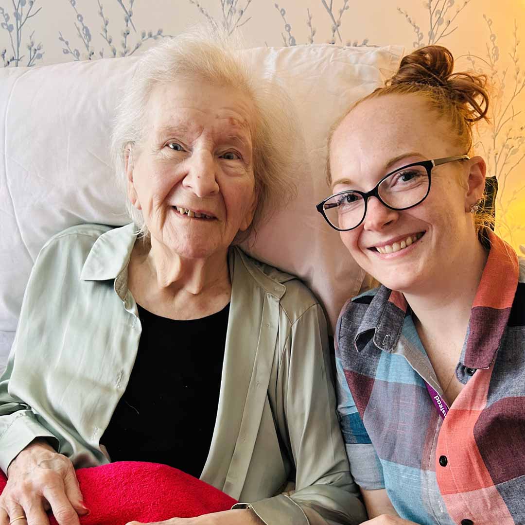 home instead client Rosemary sat smiling next to her carefully matched care professional
