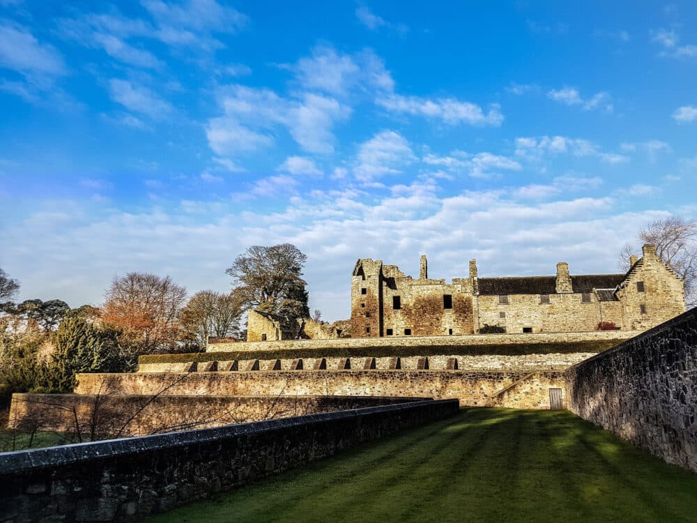 A historic stone castle ruin under a blue sky with scattered clouds, surrounded by greenery and trees. - Home Instead