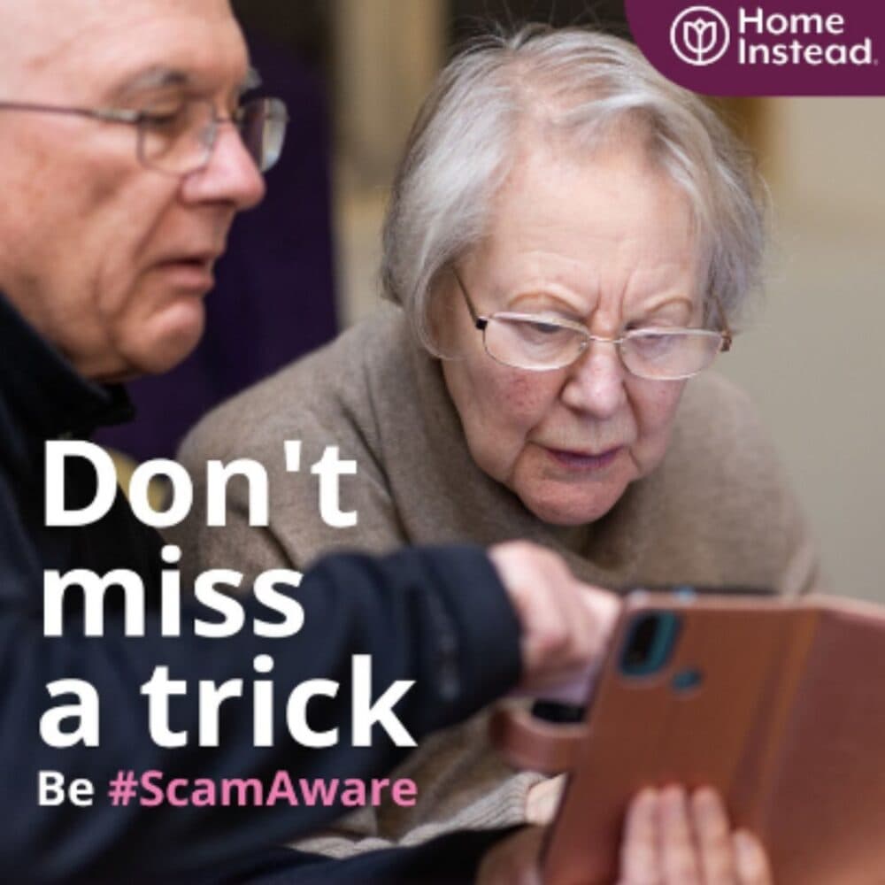 An elderly woman and a man look at a tablet. Text: "Don't miss a trick. Be #ScamAware." Home Instead logo in the corner. - Home Instead