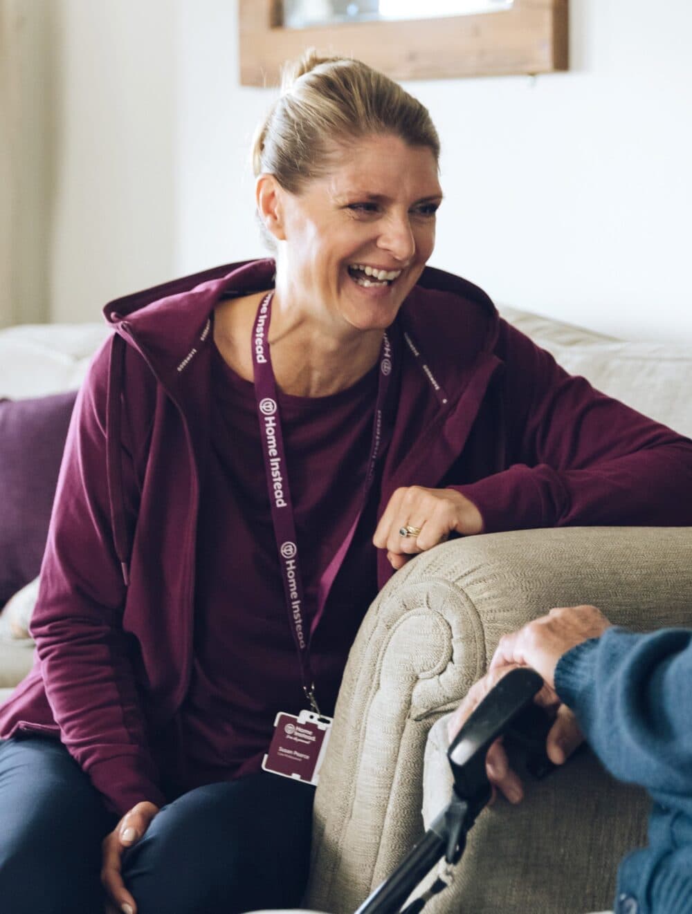 Smiling woman in a maroon hoodie sitting on a couch, engaging warmly with an elderly person. - Home Instead