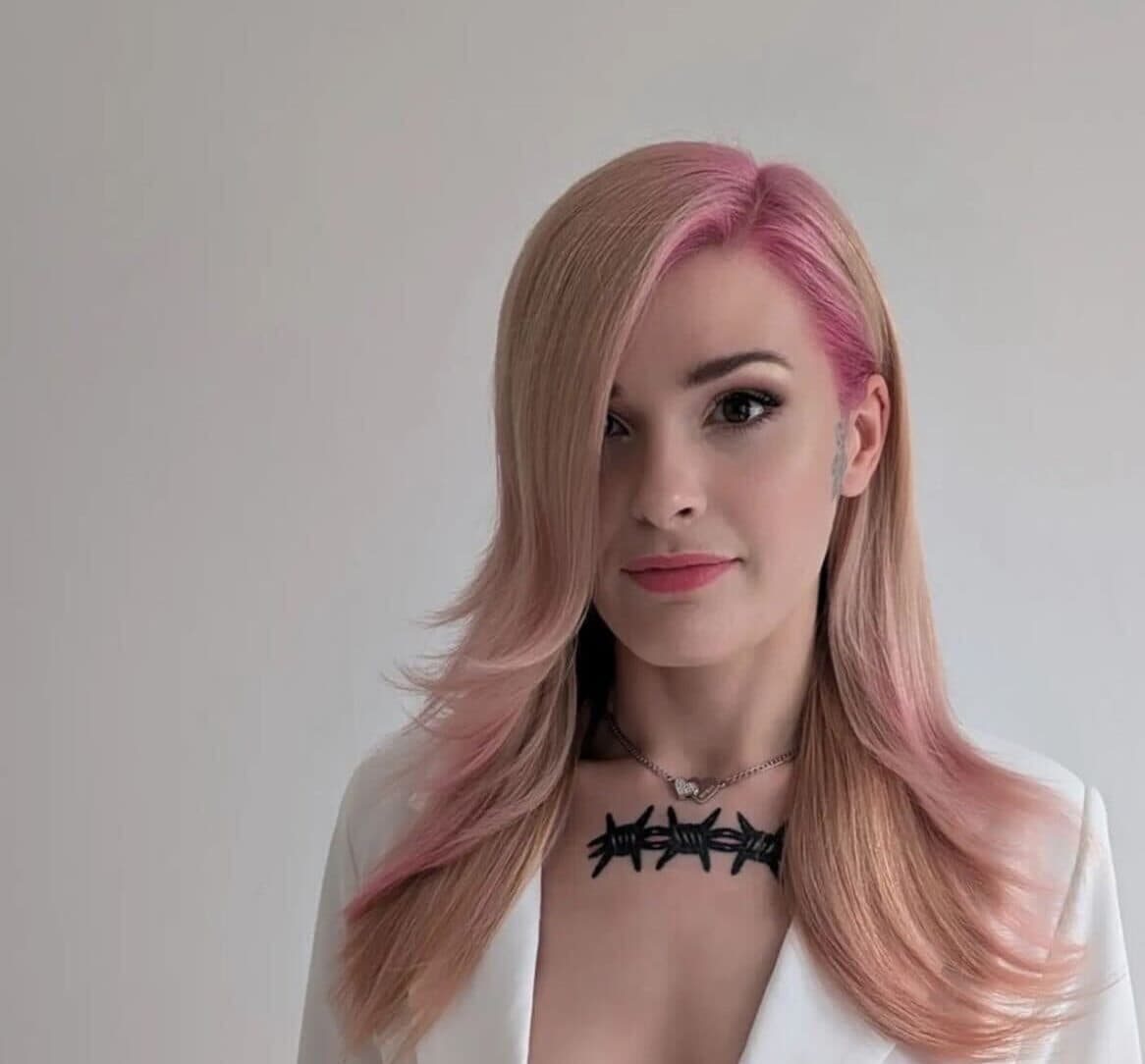 Woman with blonde and pink hair wearing a white outfit and a barbed wire necklace, standing against a plain background. - Home Instead