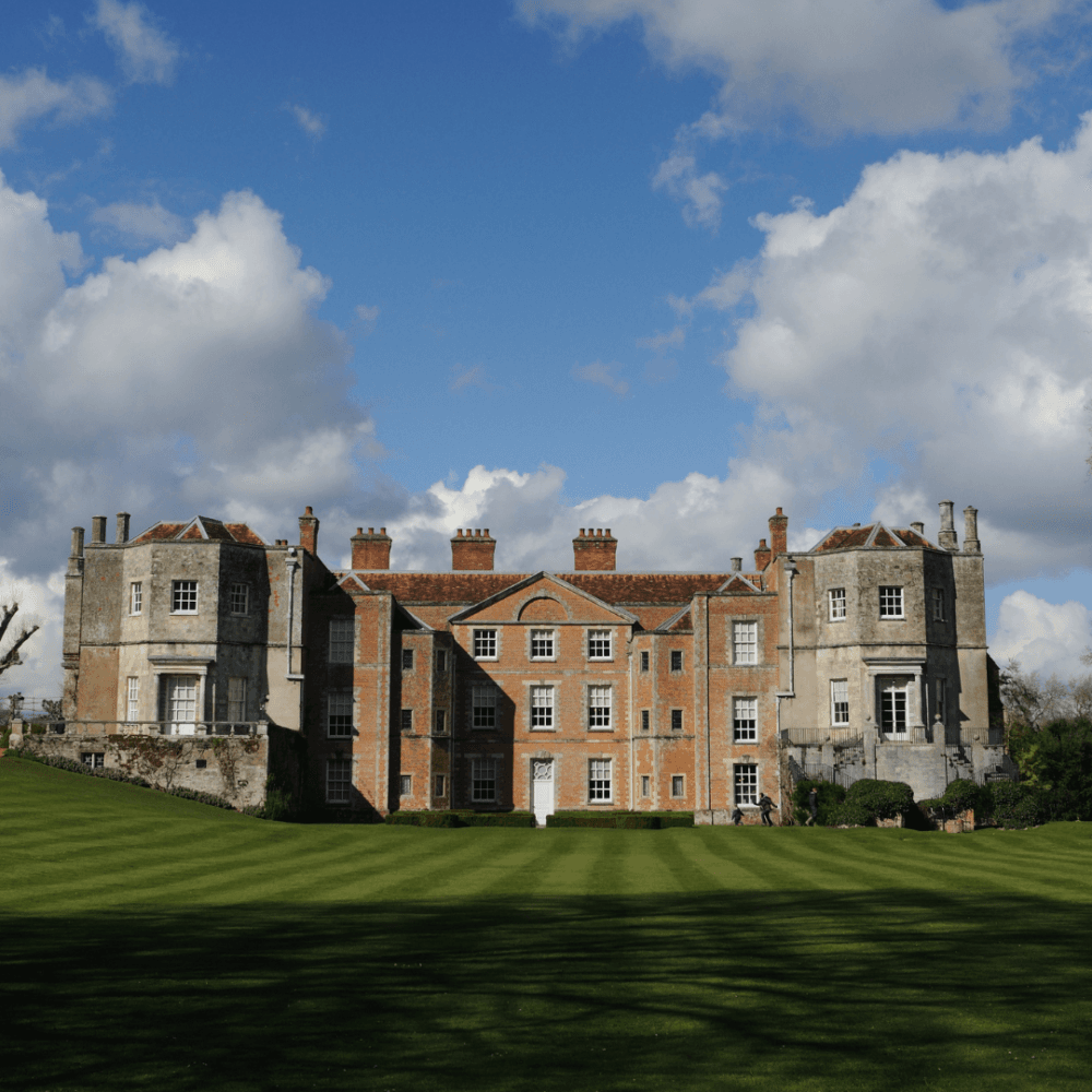 A grand historic mansion with a manicured lawn under a blue sky with clouds. - Home Instead
