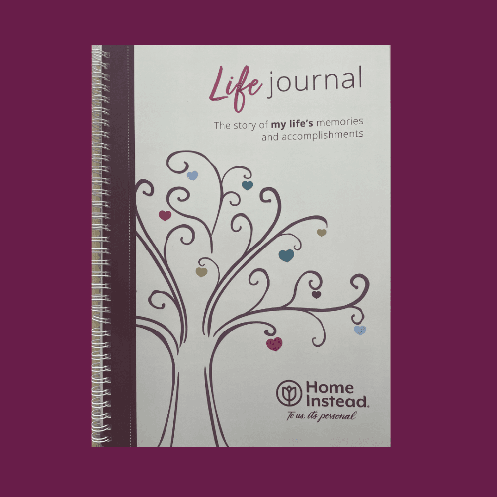 A spiral-bound "Life Journal" with a tree illustration on the cover, by Home Instead, against a maroon background. - Home Instead