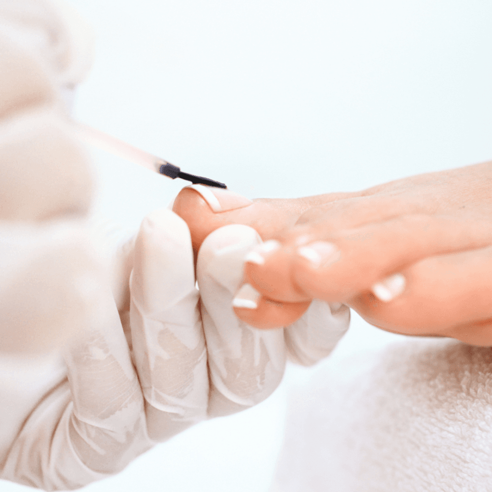 Close-up of a person receiving a pedicure with white nail polish being applied to toenails by gloved hands. - Home Instead